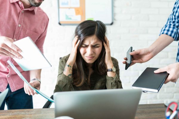 Stressed businesswoman surrounded with male colleagues assigning work at office